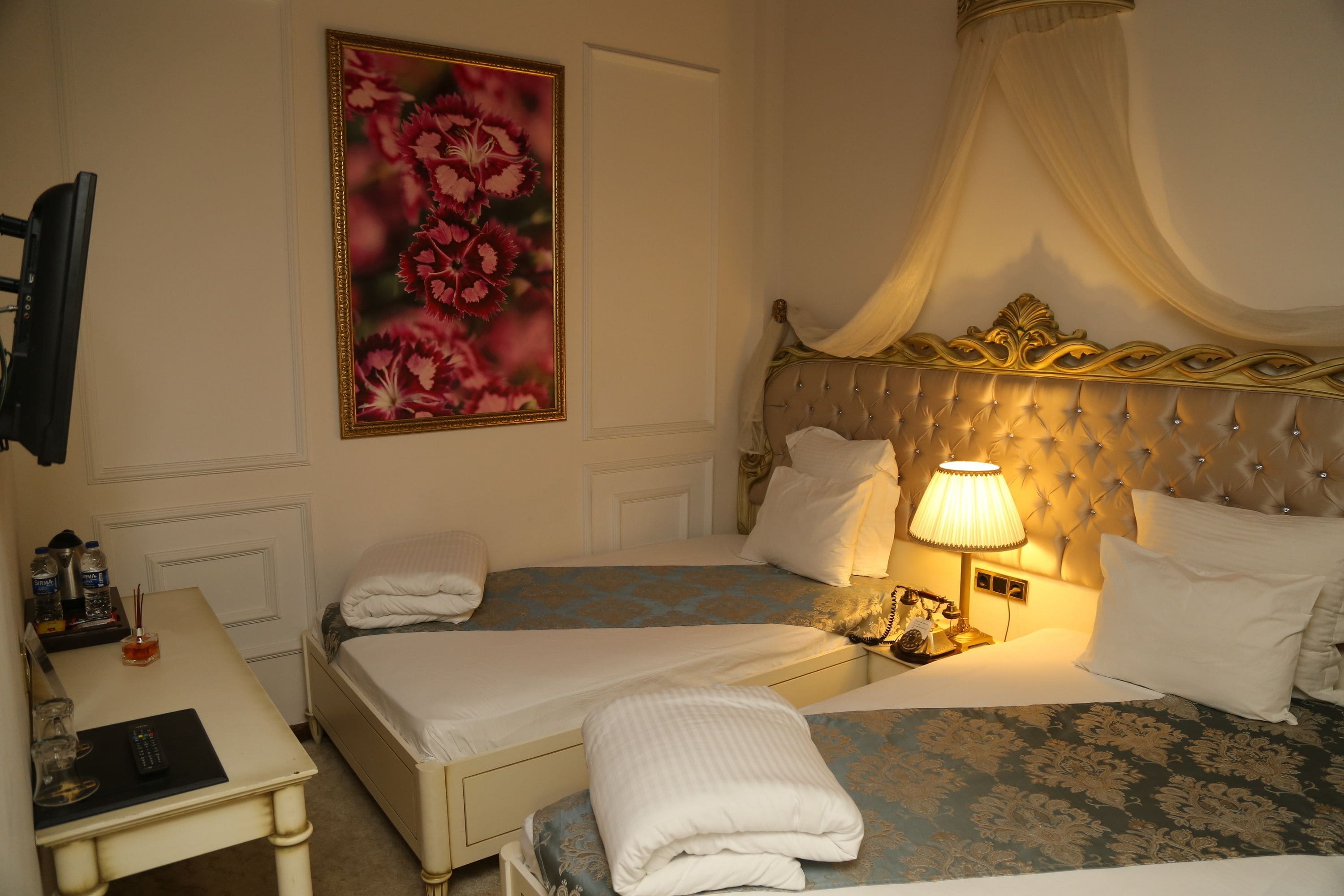 Une chambre d’hôtel avec deux lits, une table de chevet avec une lampe, une télévision et un grand tableau représentant des fleurs accroché au mur.