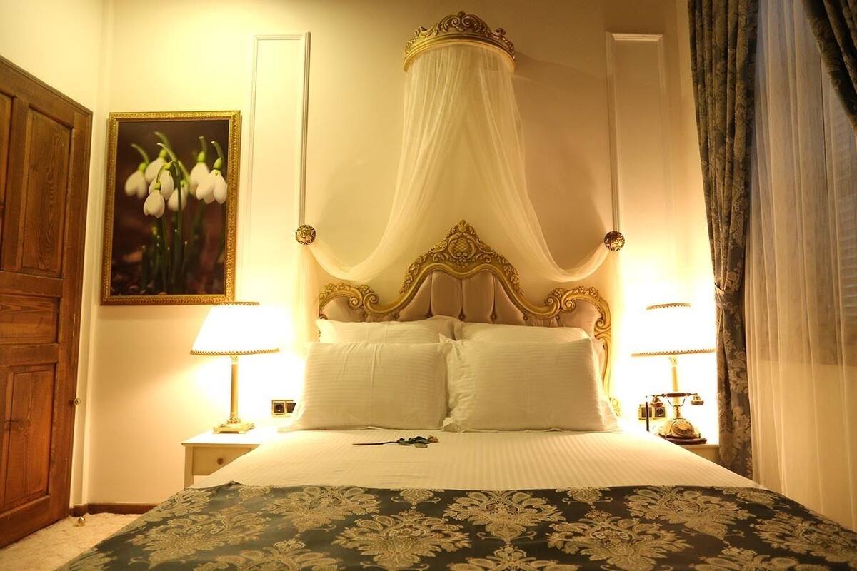 A four-poster bed with a canopy, two bedside lamps, and a floral-patterned bedspread.