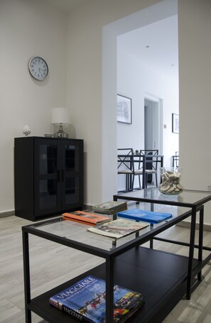 Una sala de estar moderna con una mesa de centro de vidrio que muestra libros y un mueble negro con una lámpara.