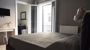 A bedroom with a bed, a bedside table with a vase of flowers, a mirror, and a view of the outside balcony. - Appartamento Cavour 37 Palermo (Palermo)