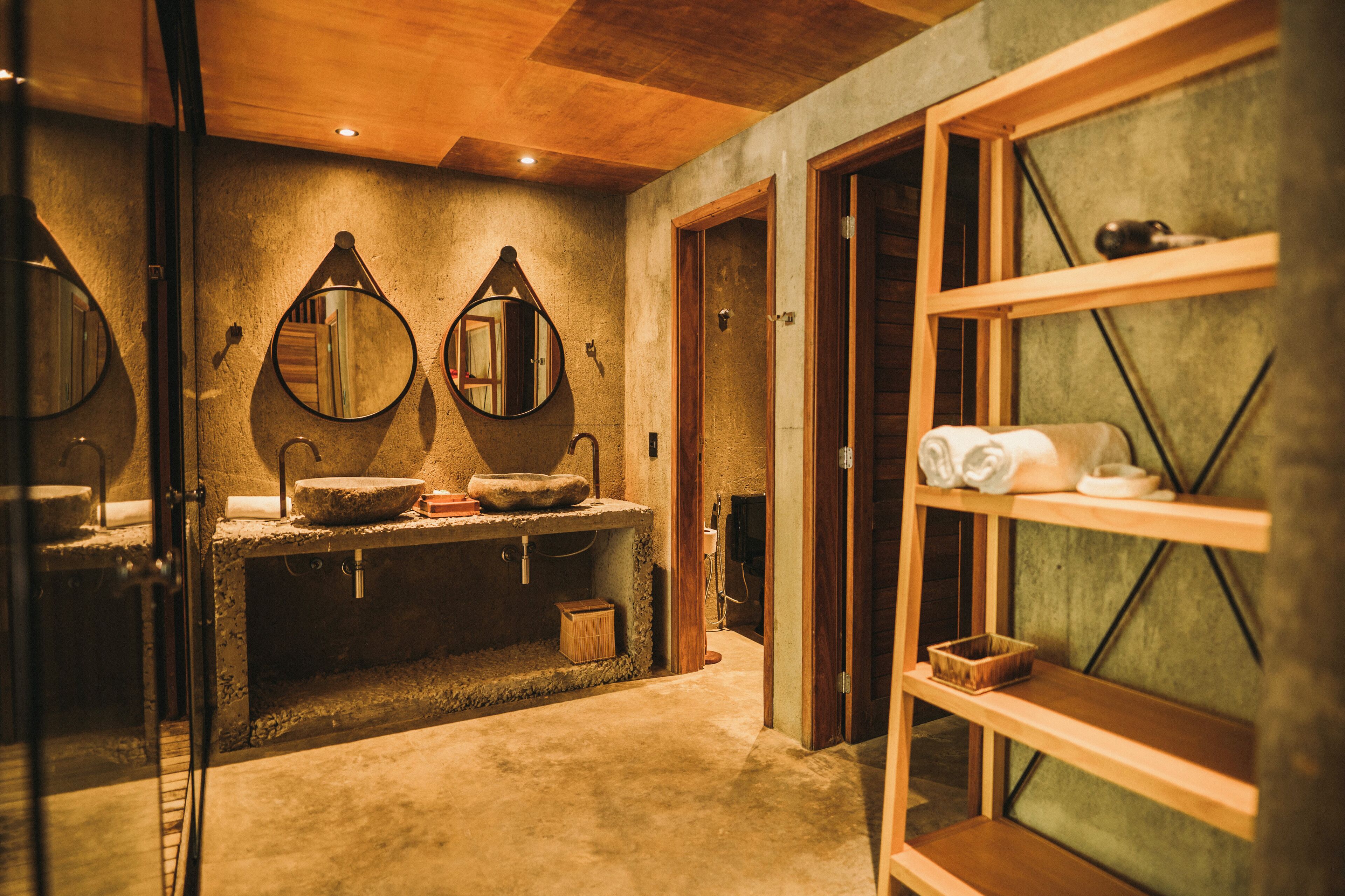 A bathroom with a stone sink, two mirrors, wooden shelves, and a towel rack.