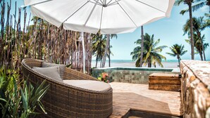 A wicker lounge chair with a cushion, a white umbrella, and a view of the beach and ocean. - Pedras Do Patacho Hotel Boutique Experience (Porto de Pedras)