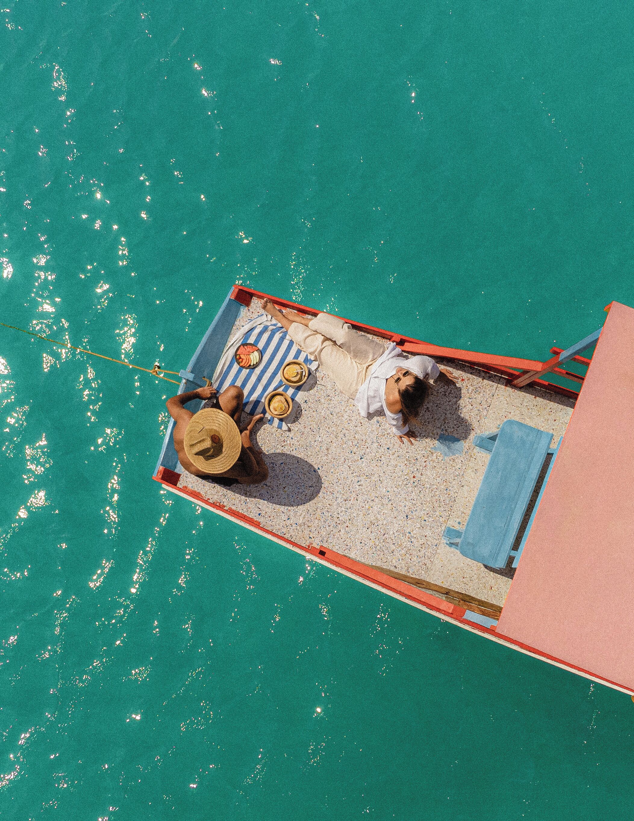An aerial view of a boat with a deck area containing a striped towel, a hat, and two bowls.