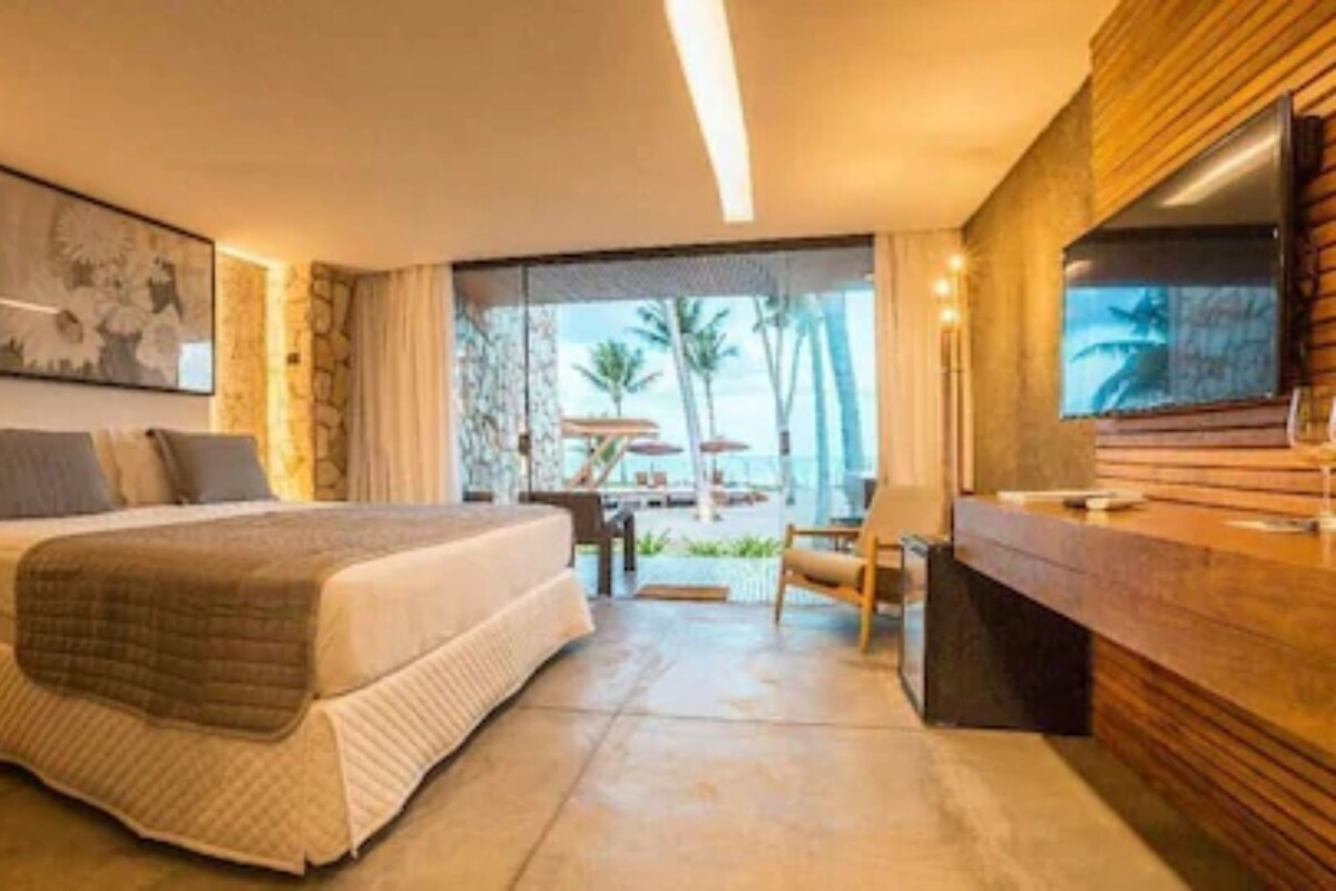 A bedroom with a bed, a desk, a chair, a TV, and a view of the outdoors.