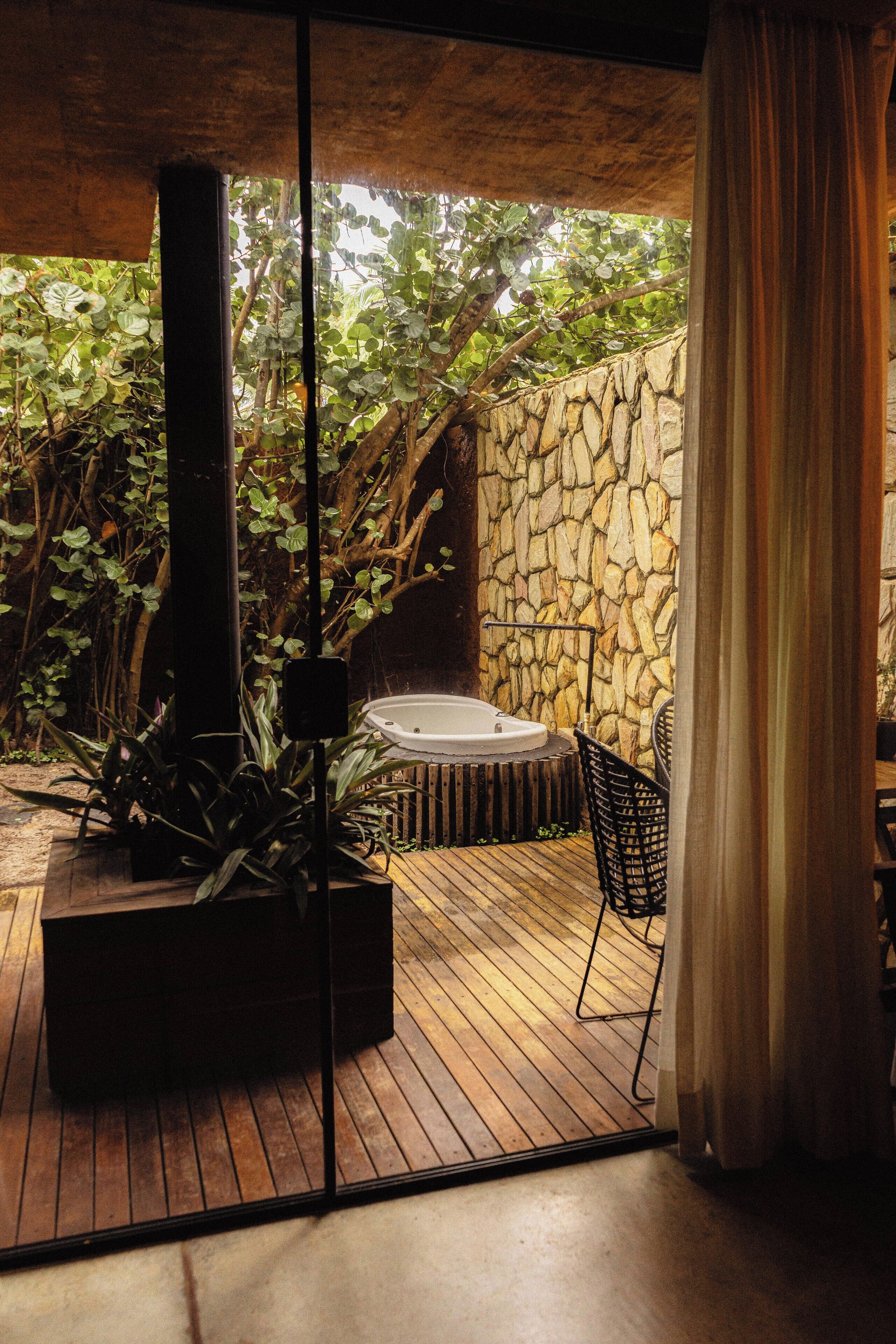 A wooden deck with a hot tub, surrounded by stone walls and lush greenery.