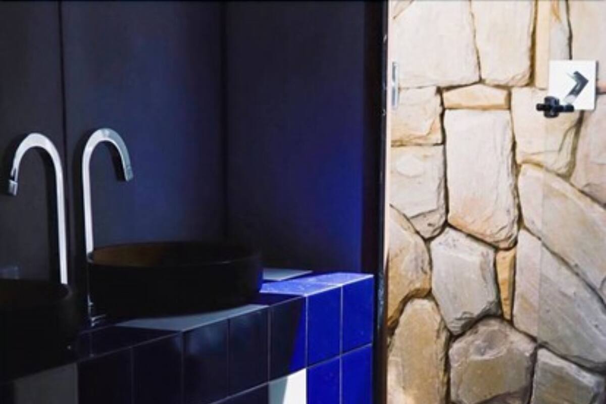 A bathroom with a stone wall, a sink with a modern faucet, and blue tiles.