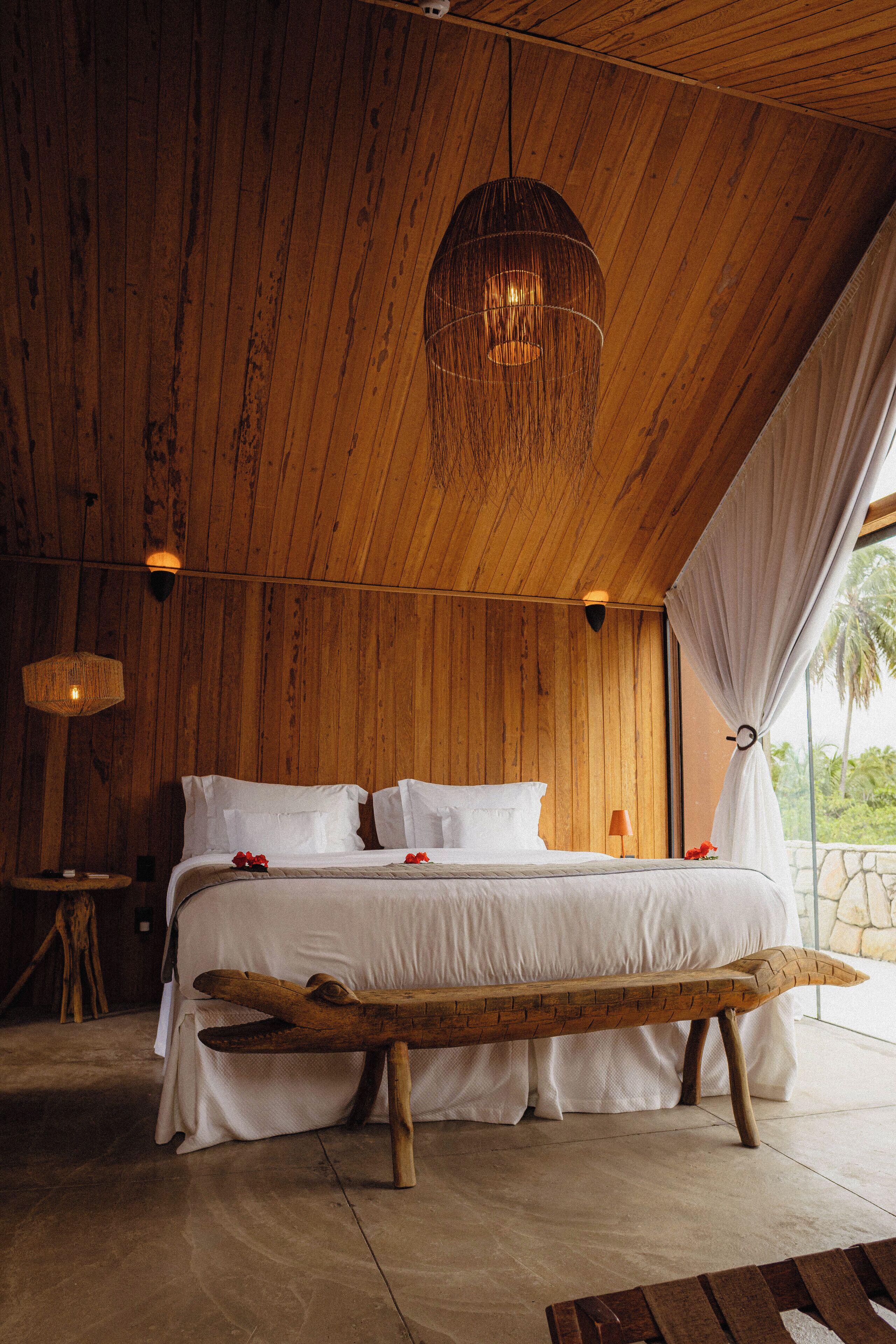 A wooden room with a bed, a bench, and a hanging light fixture.