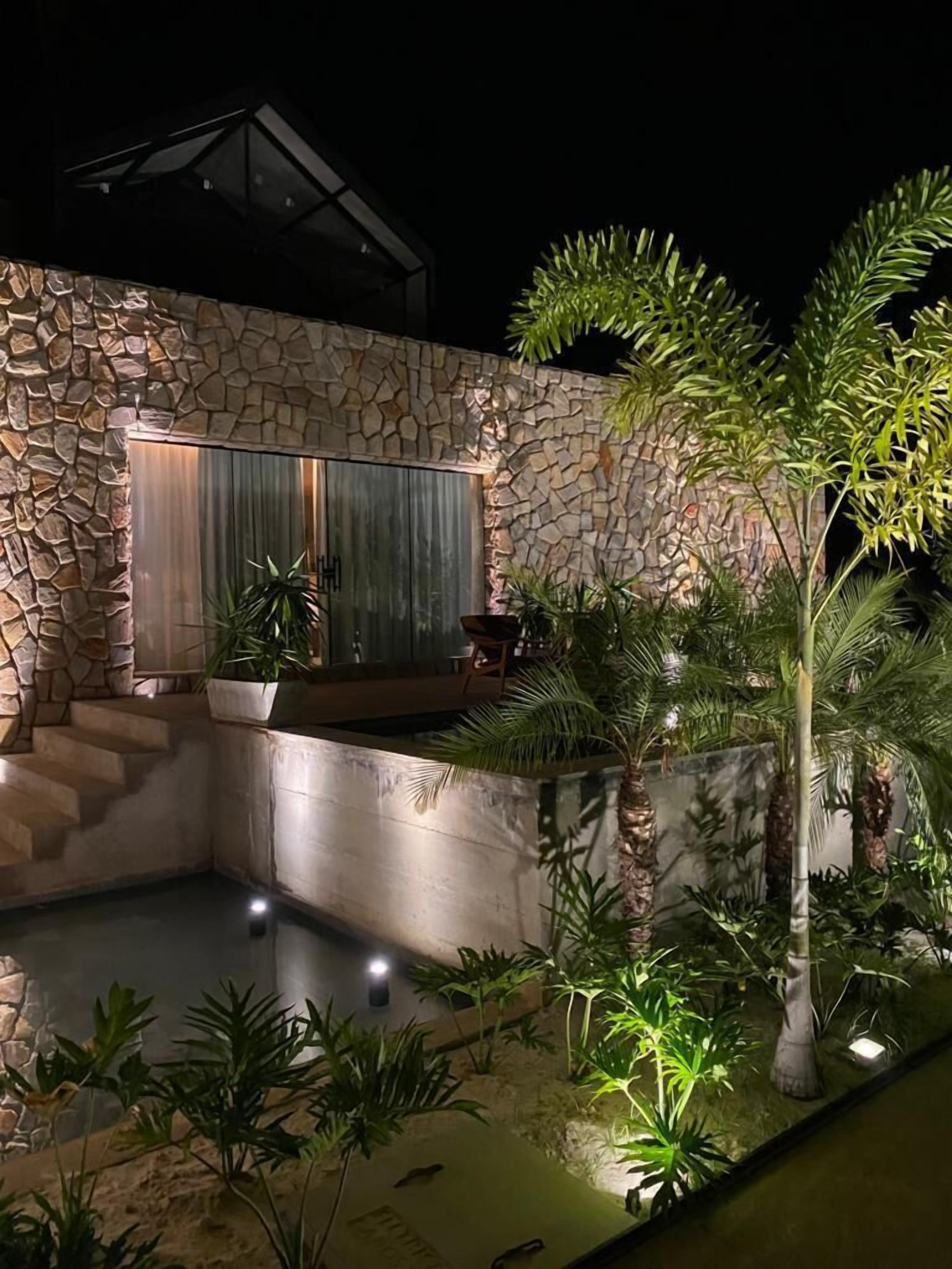 Edificio de muros de piedra con piscina, rodeado de plantas tropicales y una zona de estar.
