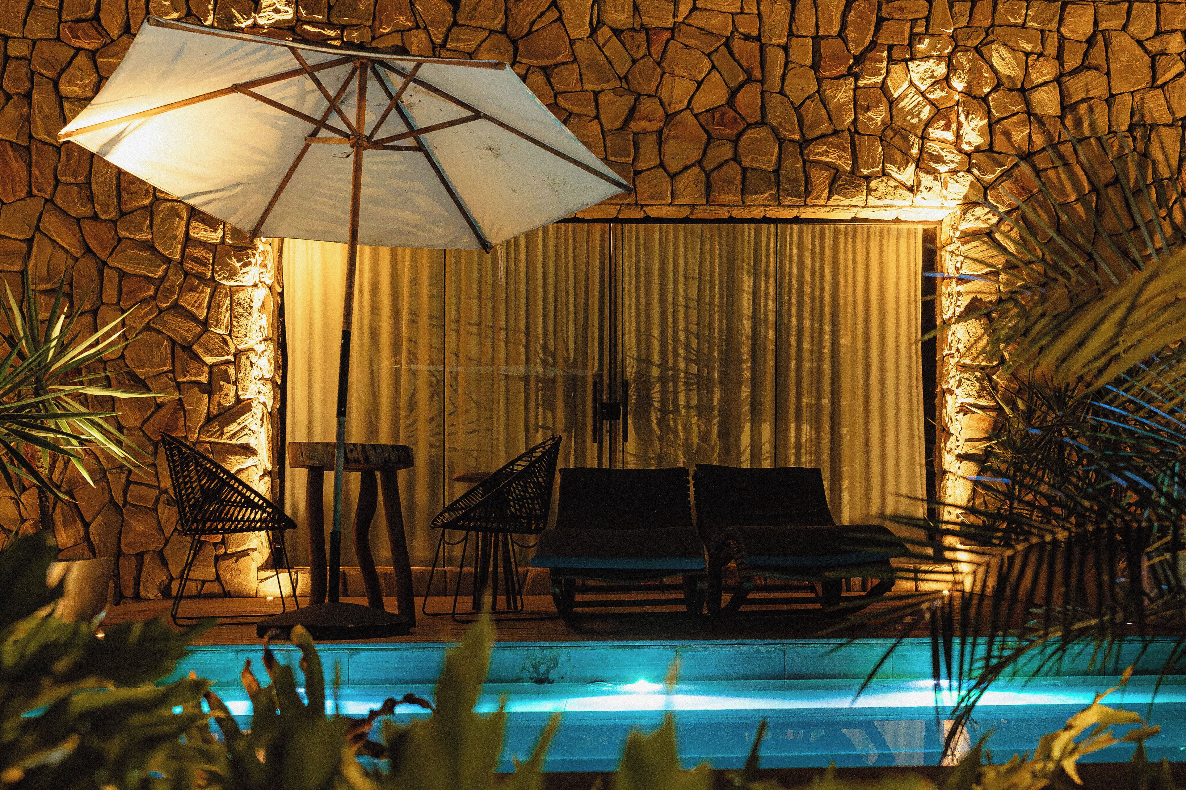 A poolside area with a stone wall, two lounge chairs, an umbrella, and a small table.