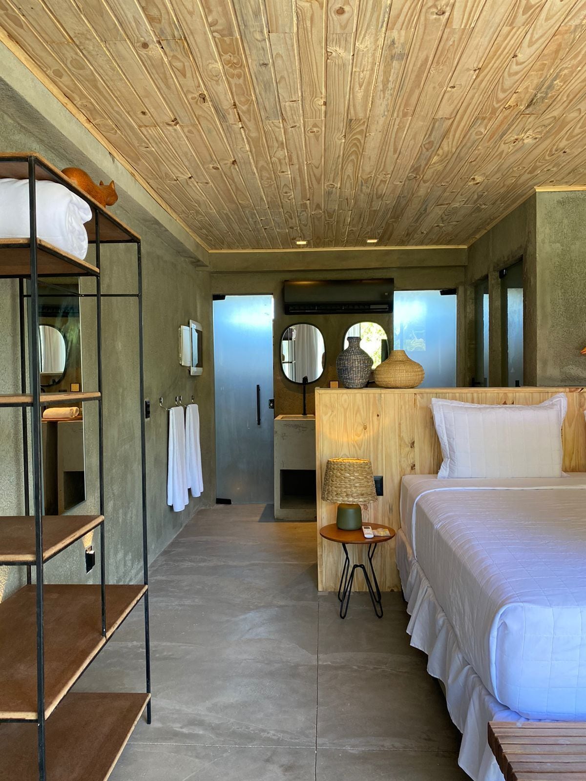 Un dormitorio moderno con techo de madera, una cama grande, un aparador de madera, un espejo y una repisa con toallas.