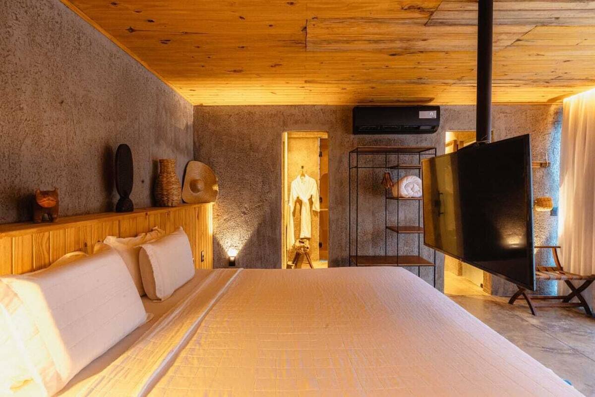 A bedroom with a large bed, wooden ceiling, stone walls, and a flat-screen TV.