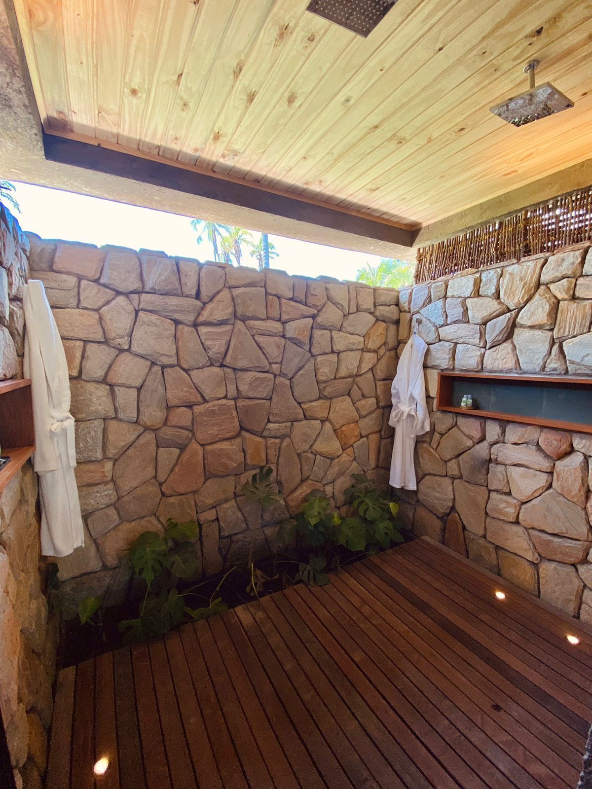 A stone-walled bathroom with a wooden floor, a shower area, and a shelf with towels.