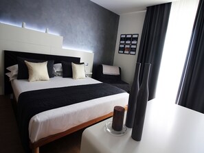 Habitació d'hotel moderna amb un llit gran, un altre més petit, una taula de nit amb espelmes i vistes a la ciutat a través de grans finestres.