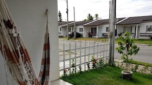 A hammock on a balcony, a small garden with a potted plant, and a view of a street with houses. - Casa póxima ao Aeroporto e UFAL (Maceió)
