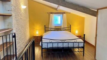 A bedroom with a sloped ceiling, a bed with a metal frame, two bedside lamps, and a window with curtains.