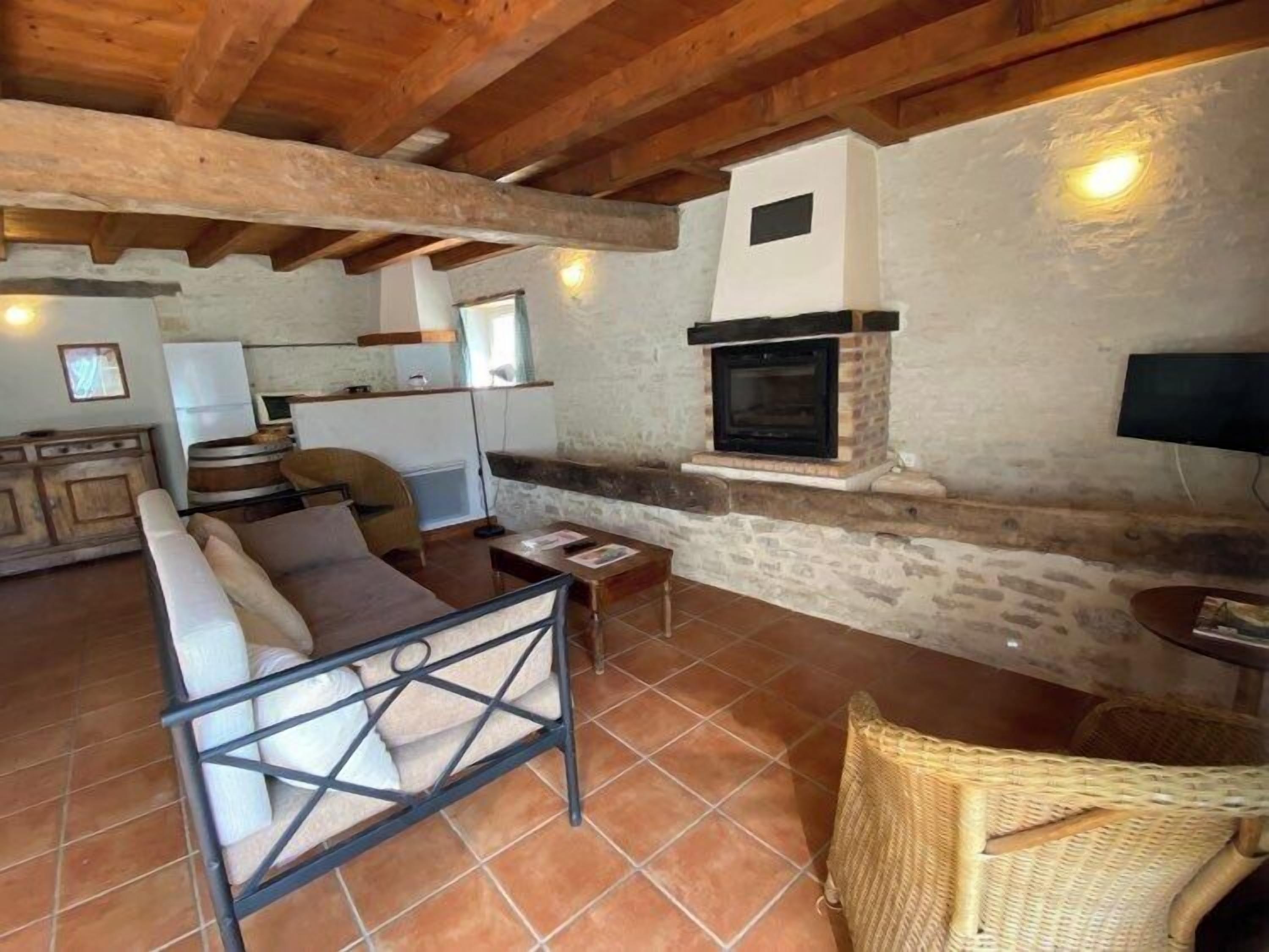 A rustic interior with exposed wooden beams, a stone fireplace, a sofa, and a wicker chair.