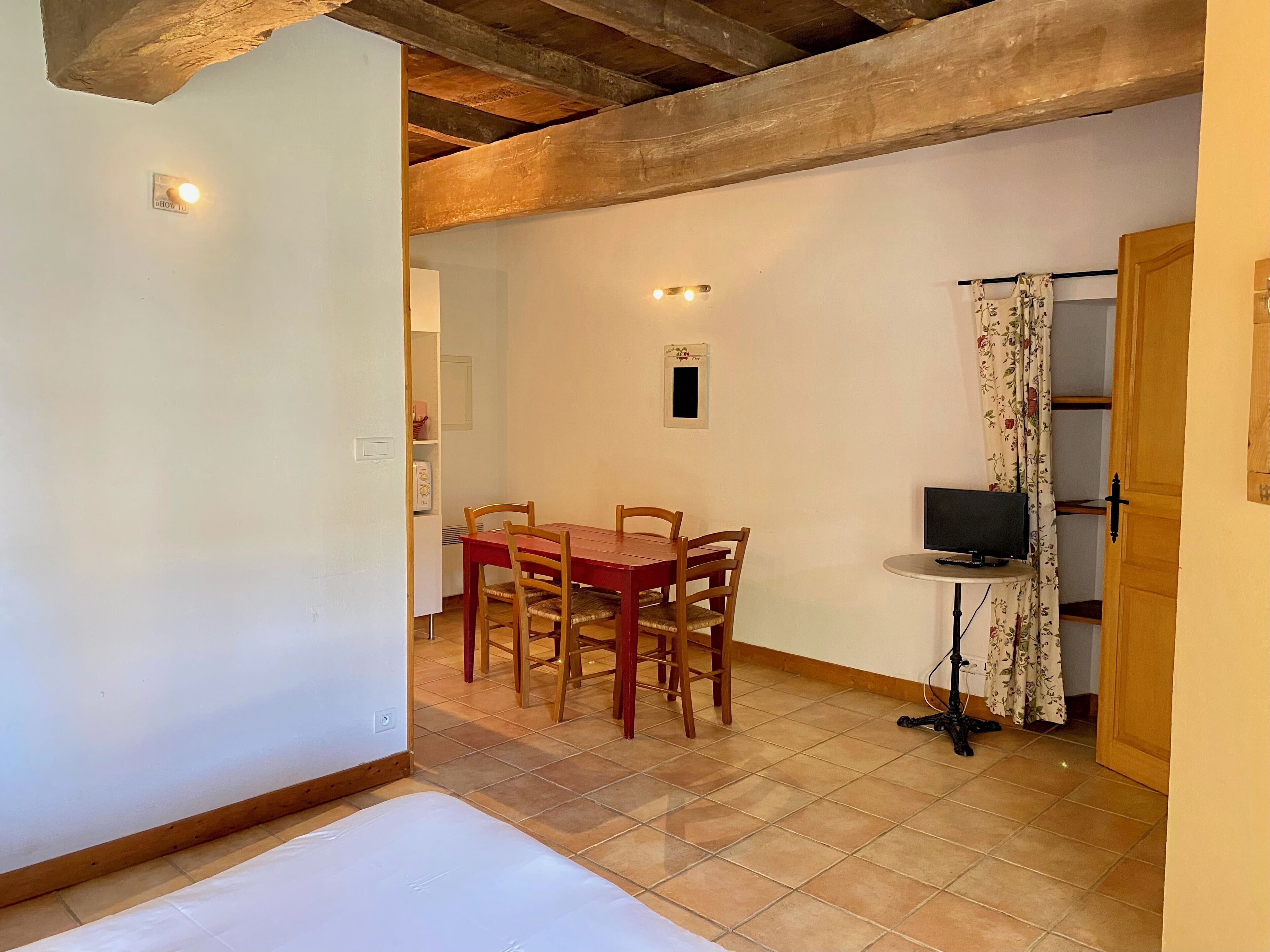 Un comedor con una mesa y sillas de madera, un televisor pequeño sobre un mueble bajo, y una puerta que da a otra habitación.