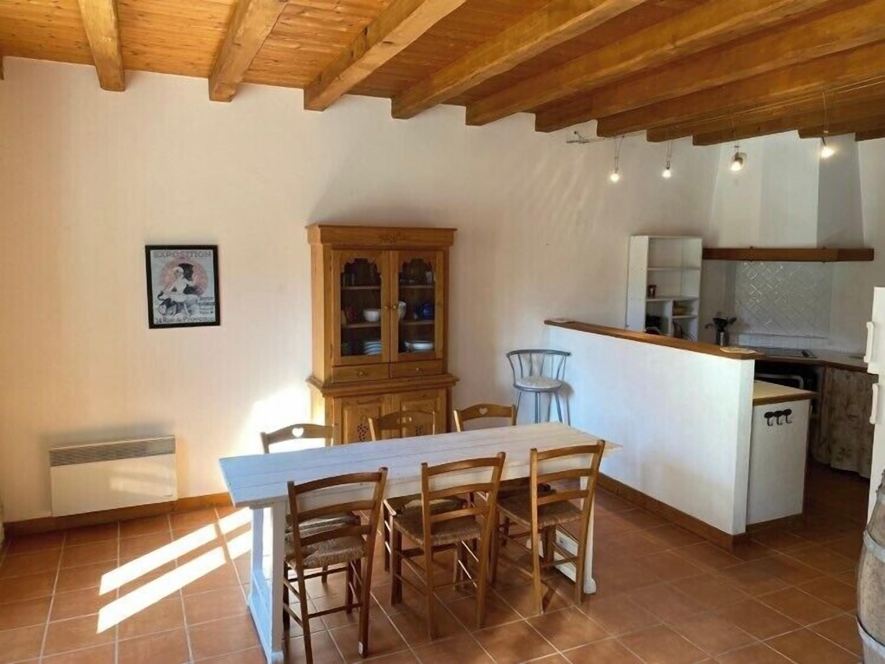 Un comedor con mesa y sillas de madera, un aparador con puertas de vidrio y una zona de cocina con encimera y electrodomésticos.