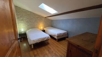 A small, cozy room with two single beds, a wooden floor, a sloped ceiling with a skylight, and a stone wall.
