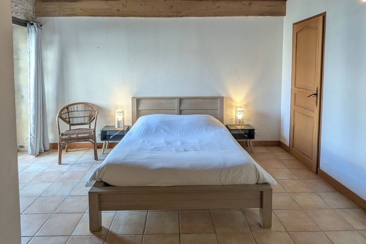 Ein Schlafzimmer mit einem hölzernen Bett, zwei Nachttischen mit Lampen, einem Korbstuhl und einer Holztür.