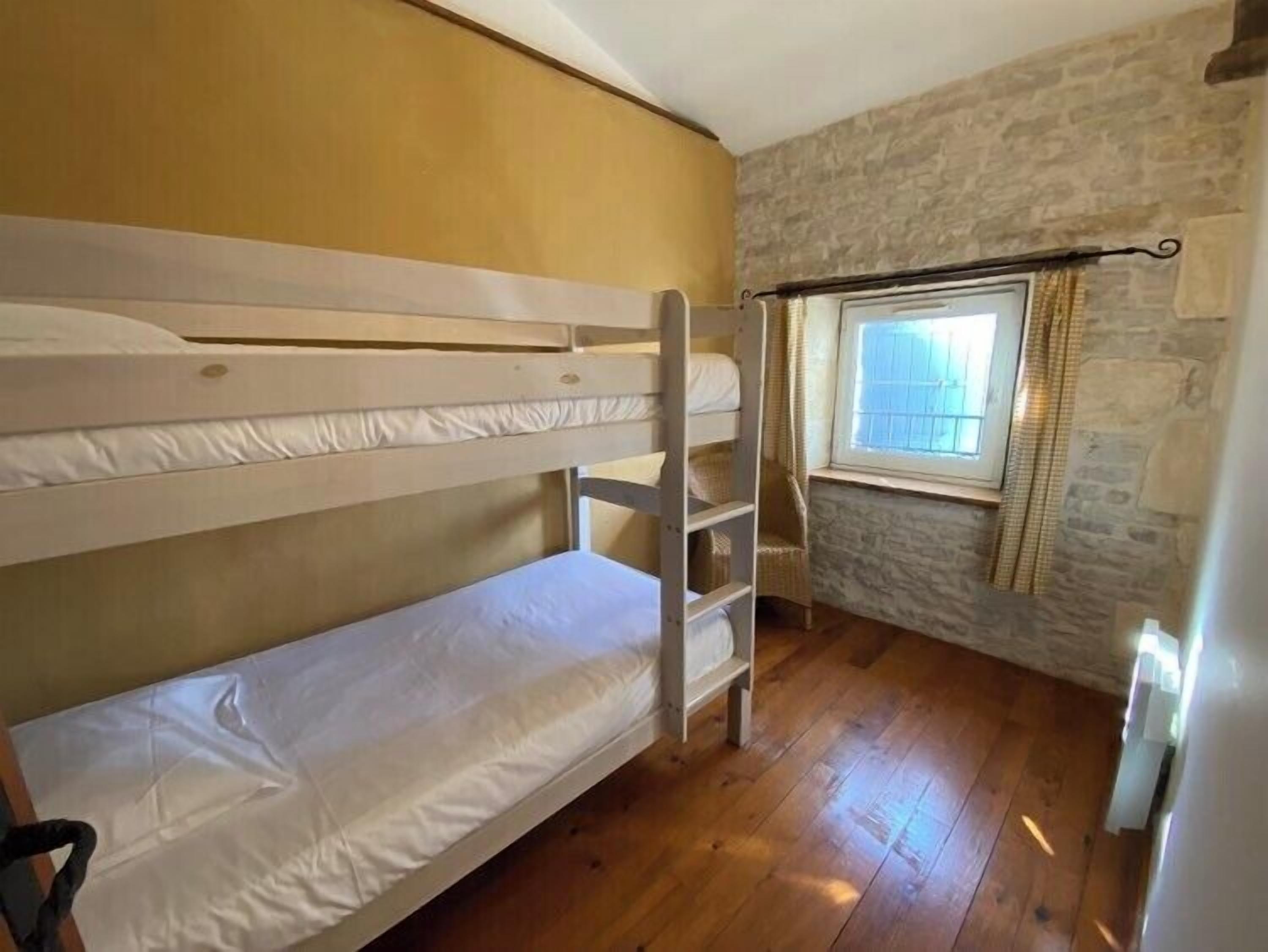 A small, cozy room with a bunk bed, a window with curtains, and a stone wall.