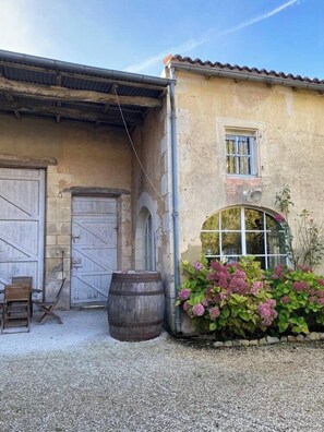Un bâtiment rustique avec une grande porte en bois, une petite fenêtre et un tonneau au premier plan.