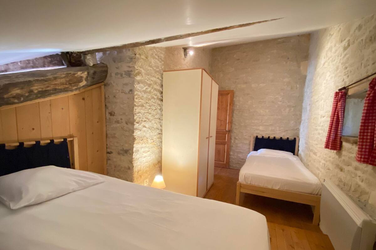 Ein Schlafzimmer mit einem großen Bett, einem kleineren Bett, einem Kleiderschrank und einer Steinwand.