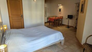 Une chambre avec un grand lit, des poutres apparentes en bois au plafond, une table à manger avec des chaises et un téléviseur dans l’espace repas.