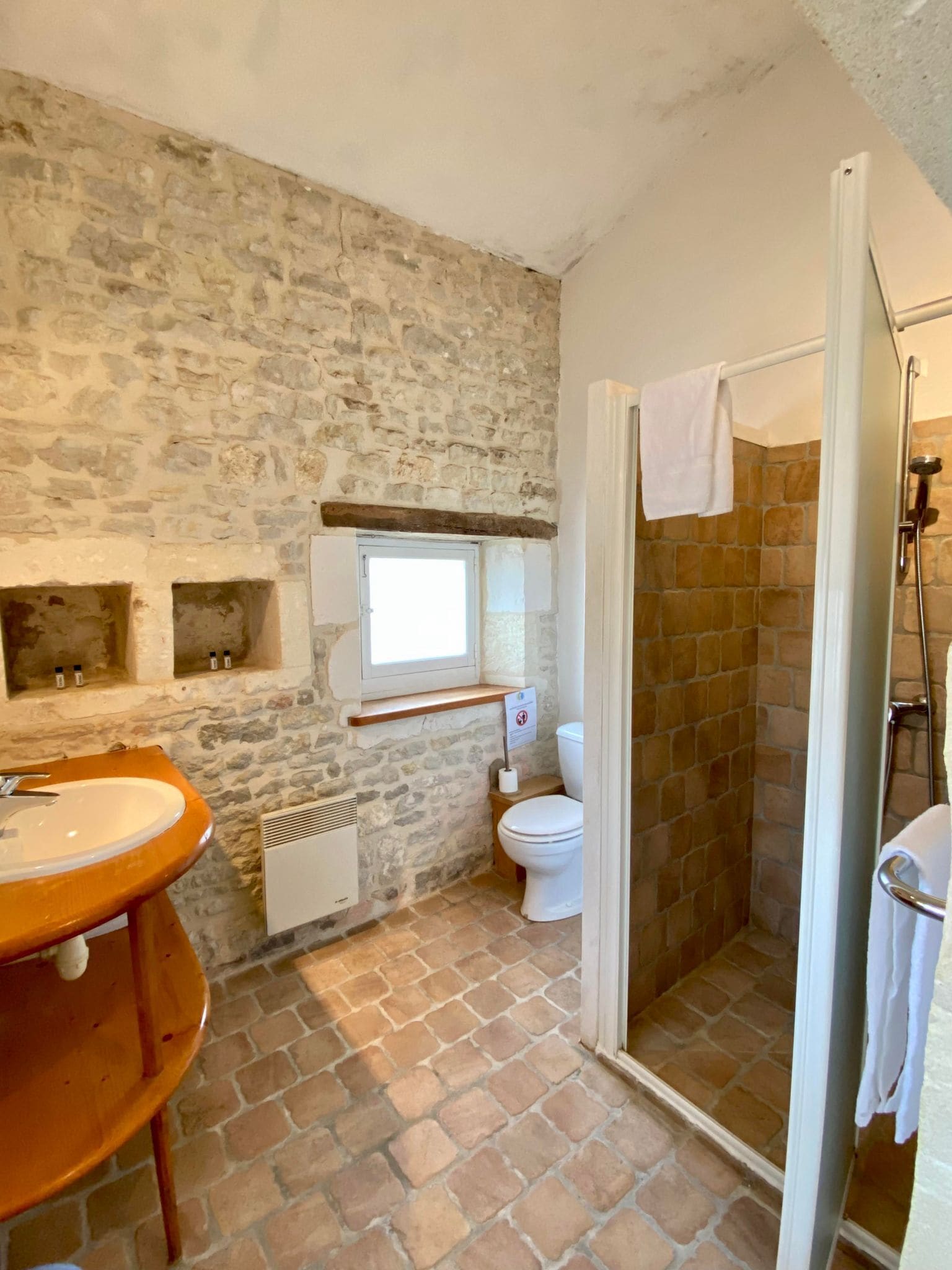A bathroom with a stone wall, a wooden sink, a toilet, and a shower area.