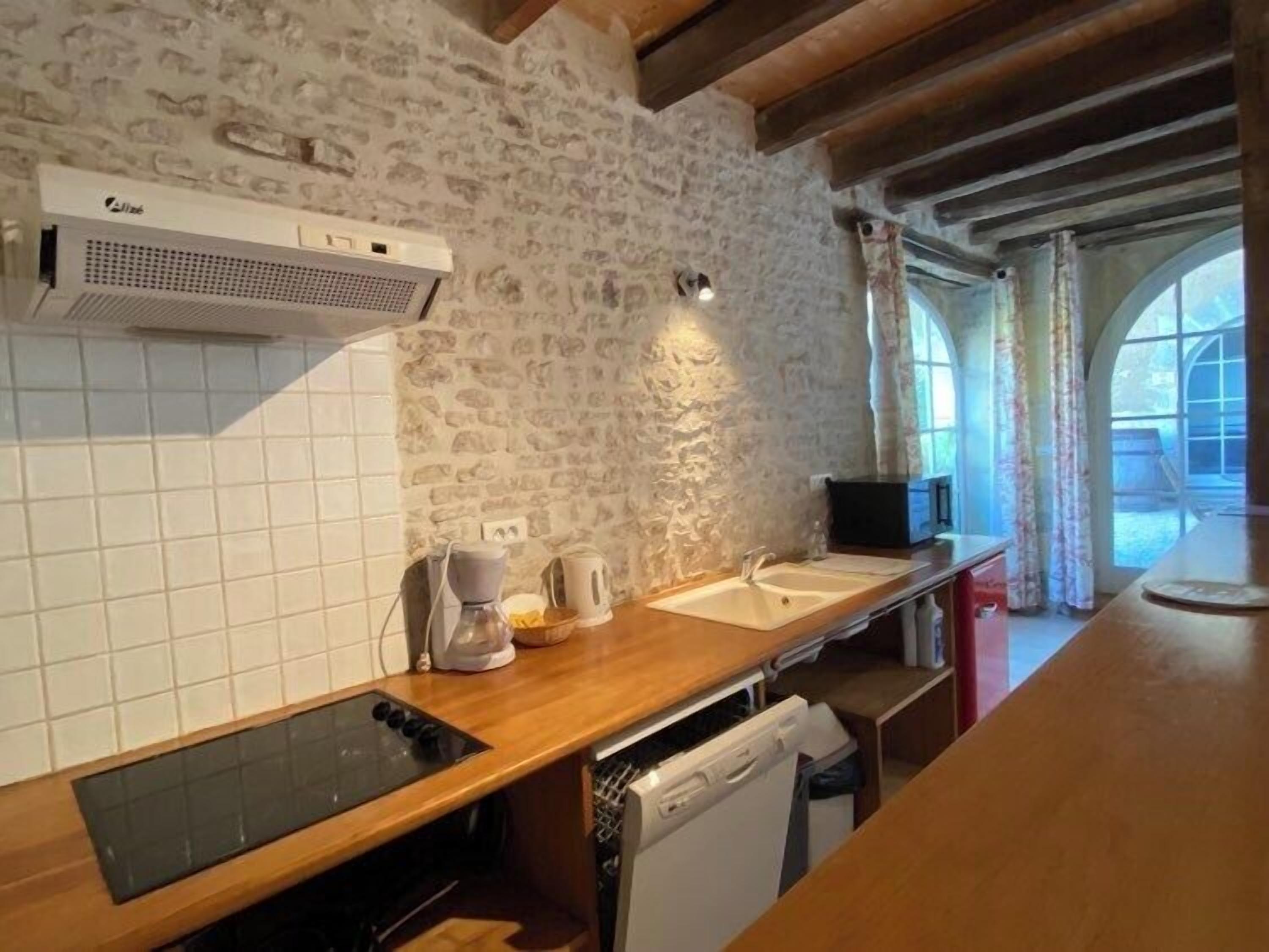 Une cuisine avec un mur en pierre, une cuisinière encastrée, un lave-vaisselle et une fenêtre avec des rideaux.