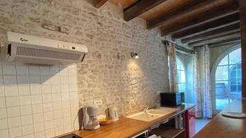 Une cuisine avec un mur en pierre, une cuisinière encastrée, un lave-vaisselle et une fenêtre avec des rideaux.