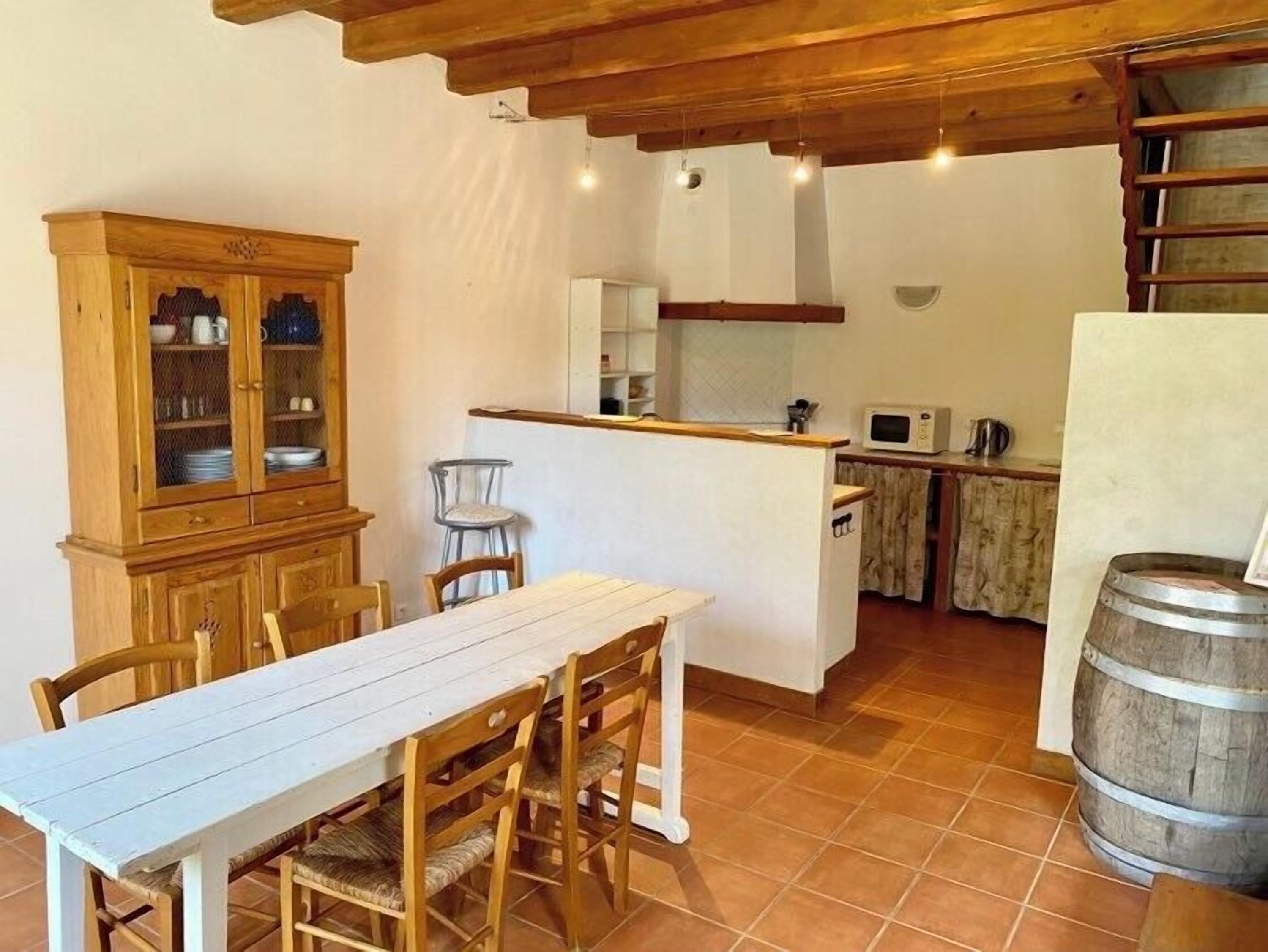 A rustic kitchen with a wooden table and chairs, a cabinet with glass doors, and a small island with a microwave.