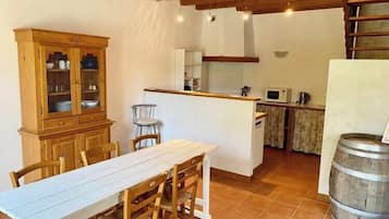 A rustic kitchen with a wooden table and chairs, a cabinet with glass doors, and a small island with a microwave.