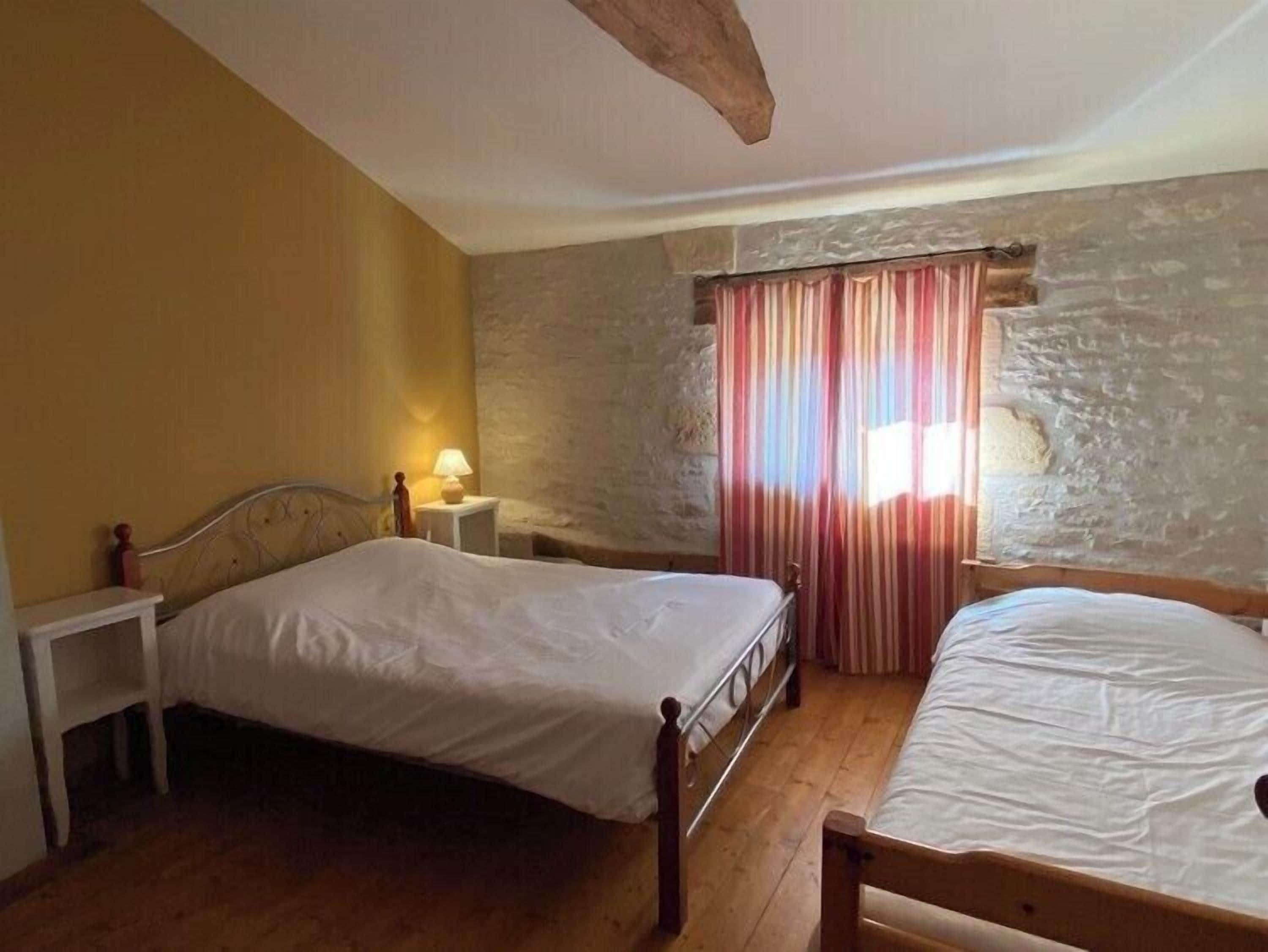 Una camera da letto con due letti, un muro in pietra, un soffitto in legno e una finestra con tende.
