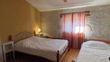 A bedroom with two beds, a stone wall, a wooden ceiling, and a window with curtains.