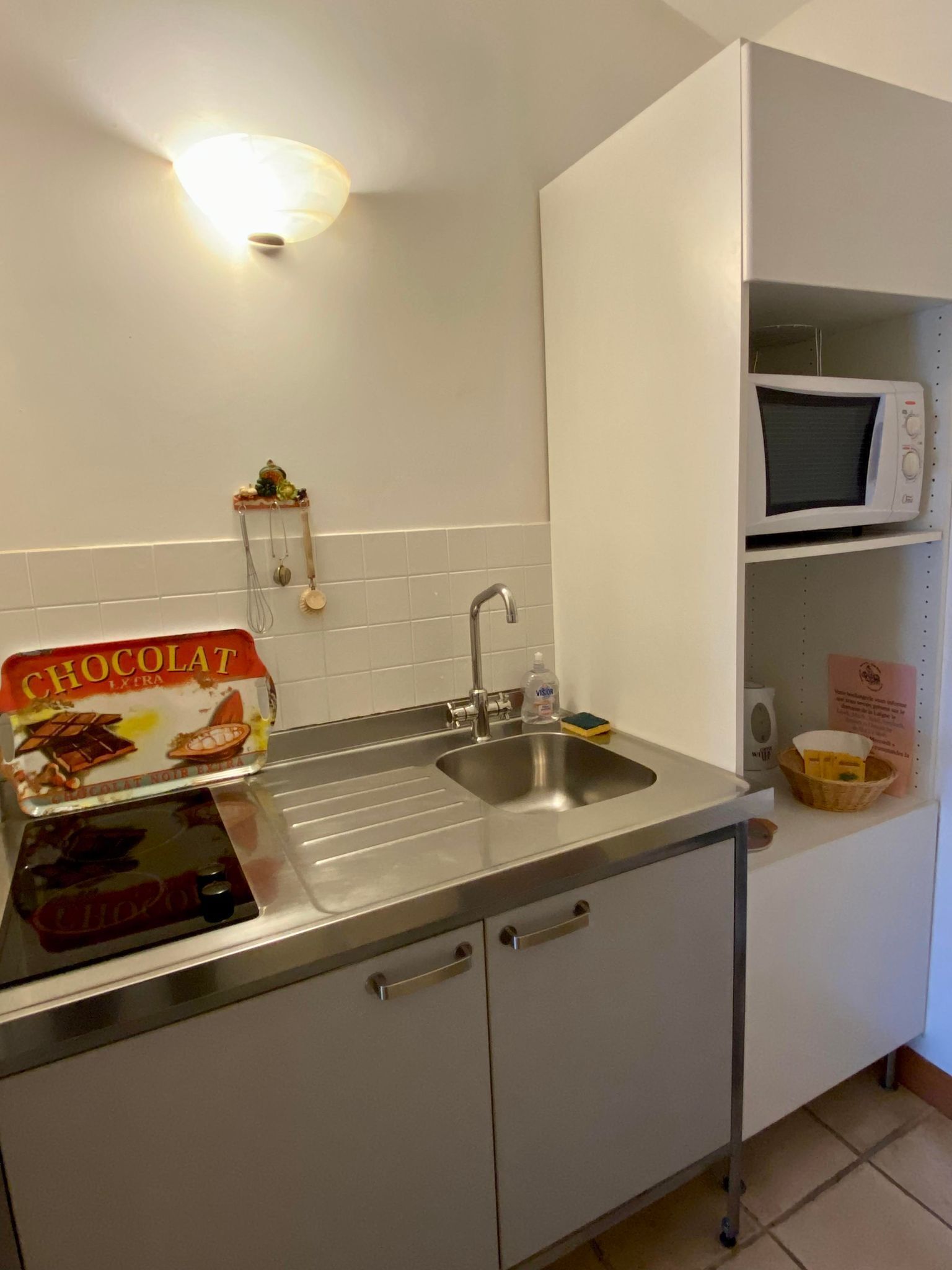 A kitchen with a stainless steel sink, a microwave, and a box of chocolate.