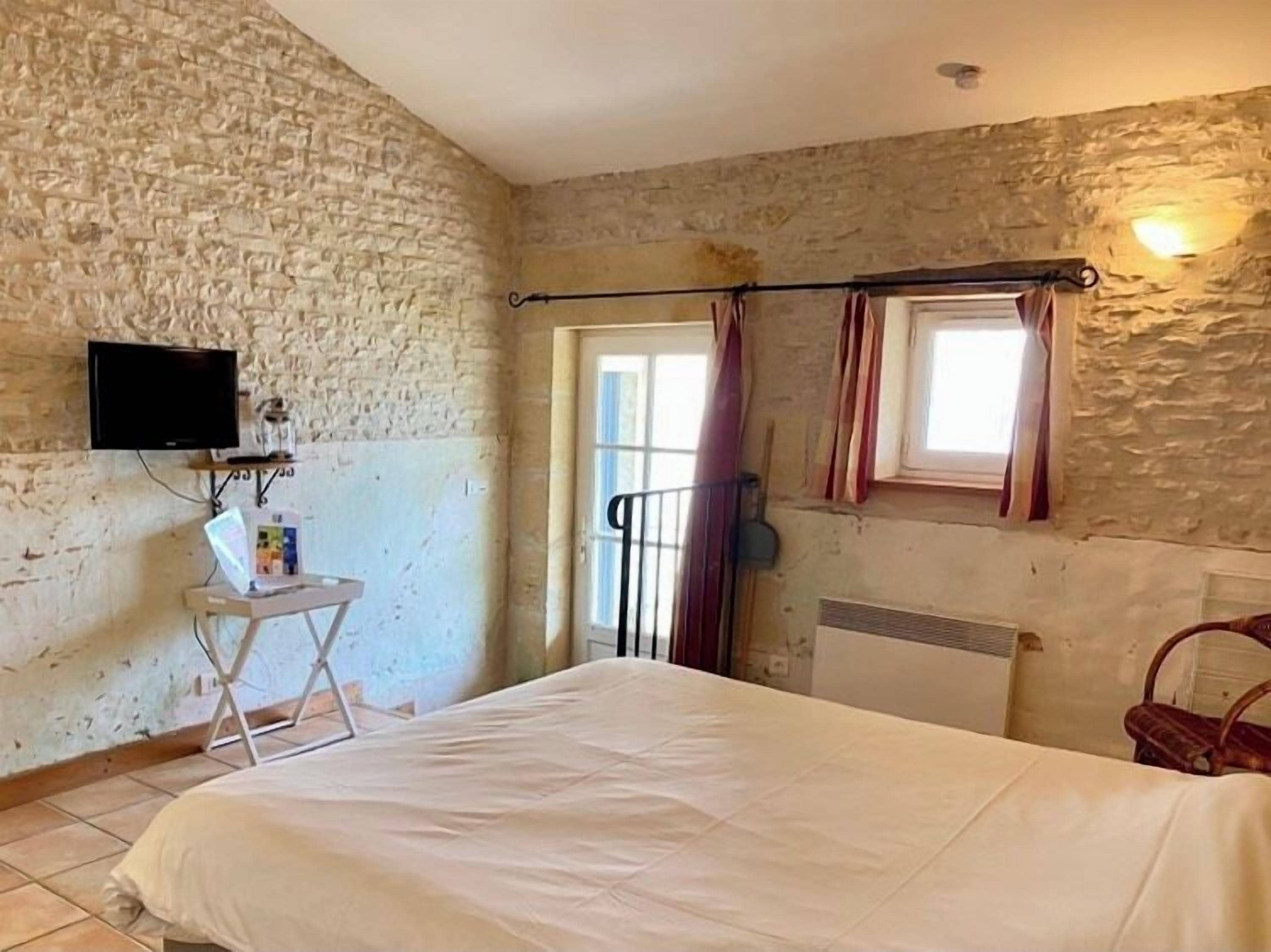 Ein Schlafzimmer mit einer Steinsandsteinwand, einem Bett, einem Fernseher, einem kleinen Tisch und einem Fenster mit Vorhängen.
