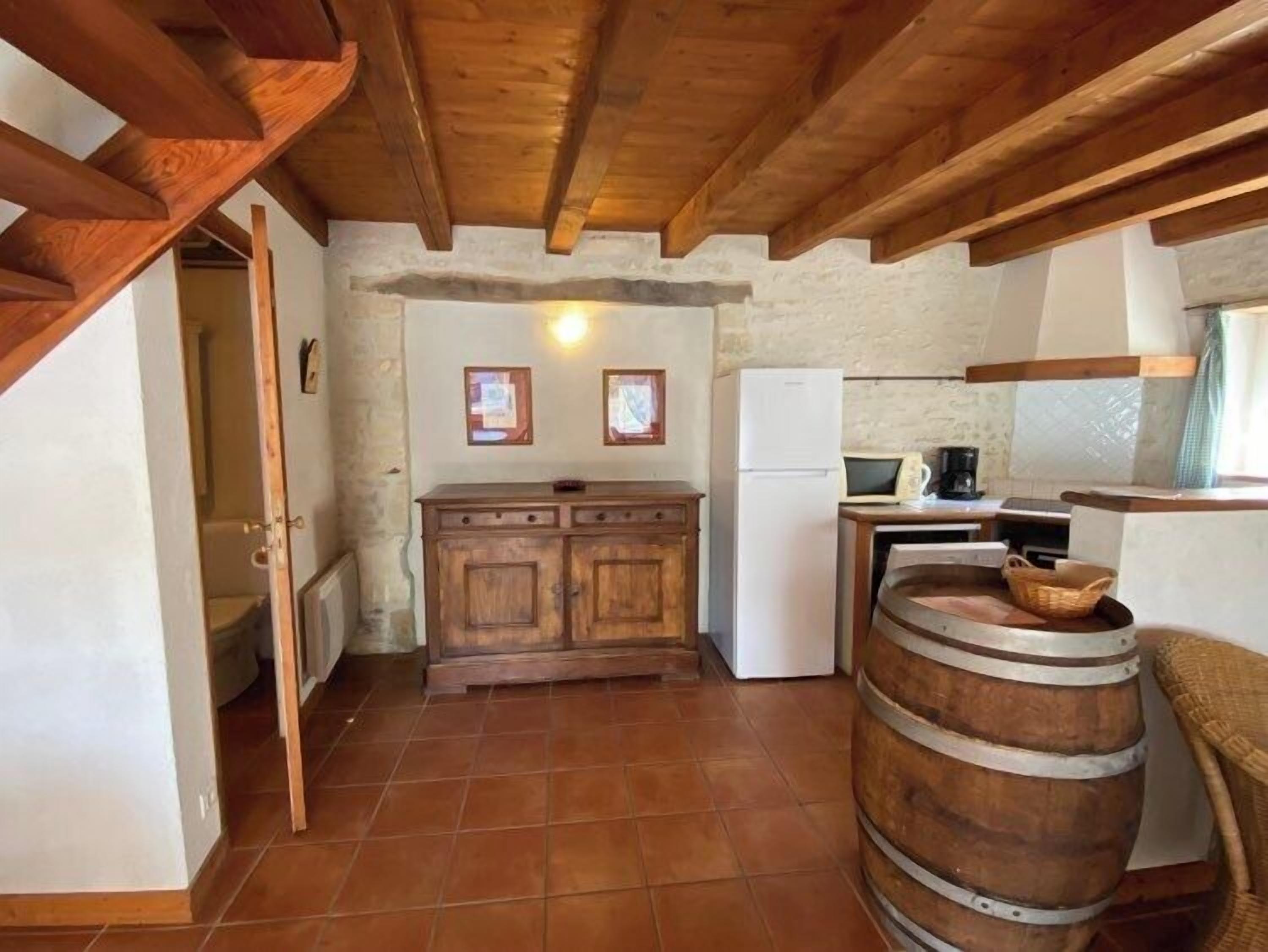 Una cucina rustica con travi in legno, pavimento piastrellato, un armadietto in legno, un frigorifero bianco e una botte di legno.