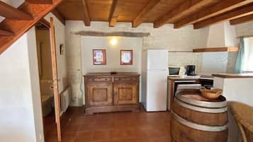 Una cucina rustica con travi in legno, pavimento piastrellato, un armadietto in legno, un frigorifero bianco e una botte di legno.