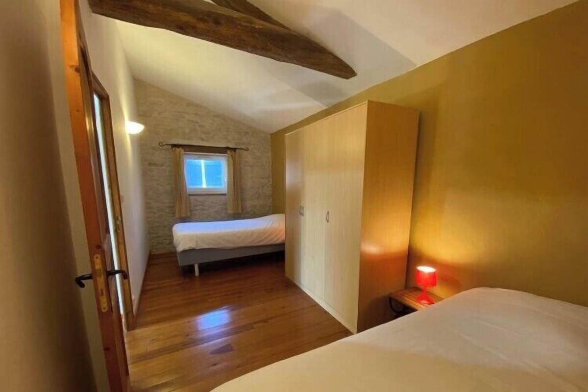 Ein Schlafzimmer mit Holzboden, einem Bett, einem Nachttisch mit Lampe, einem Kleiderschrank und einem Fenster mit Vorhängen.