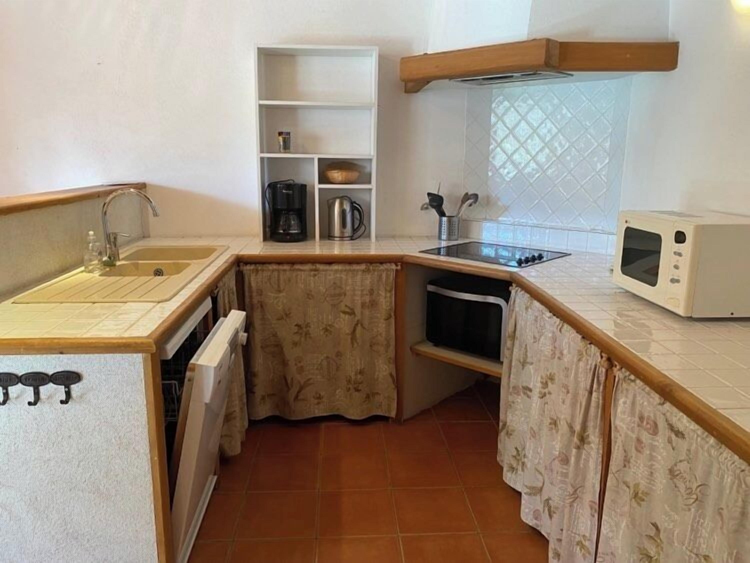 A compact kitchen with a sink, stove, microwave, and a small shelf with kitchenware.