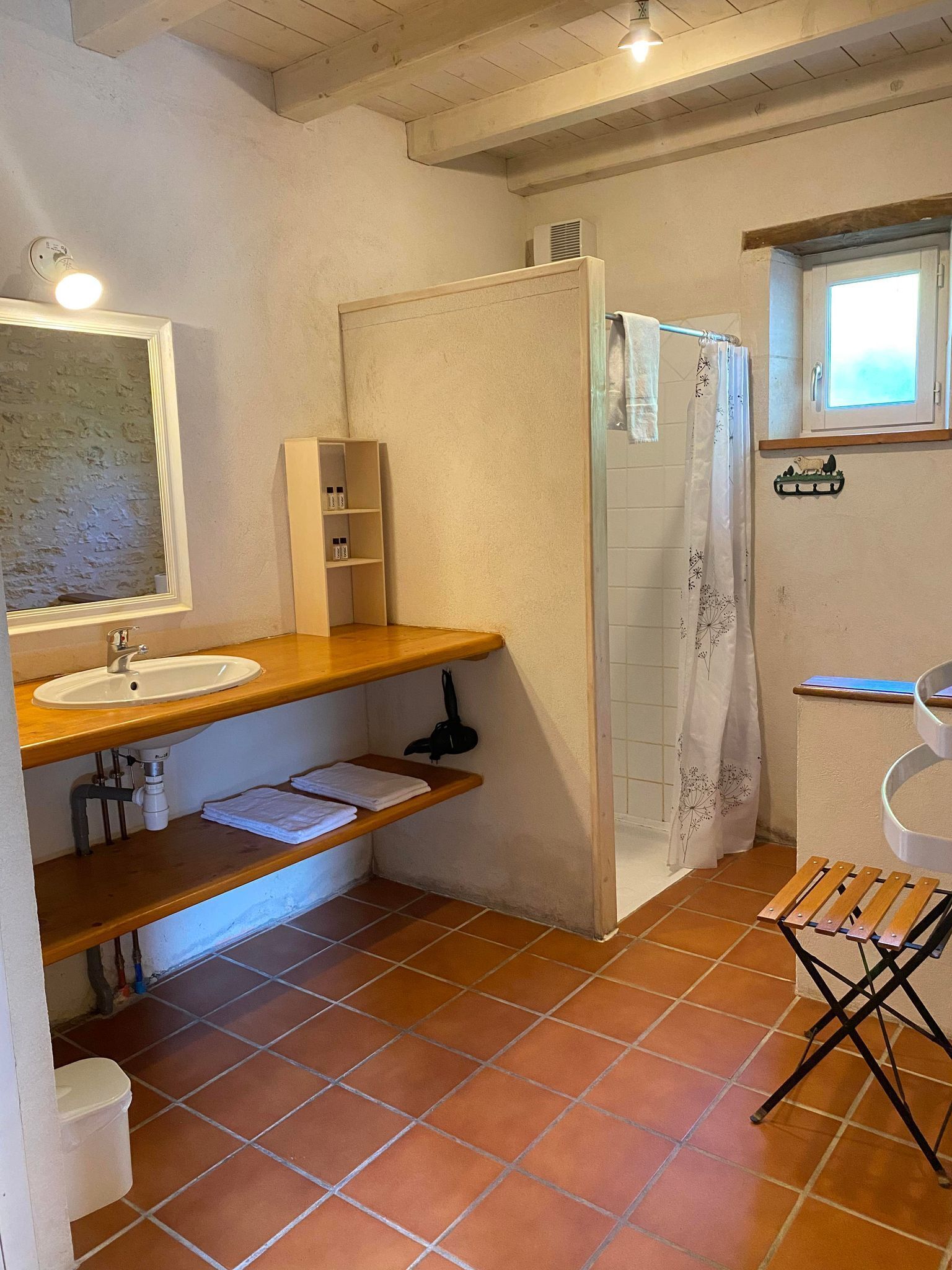 A bathroom with a wooden vanity, a white sink, a shower with a glass door, and a small window.