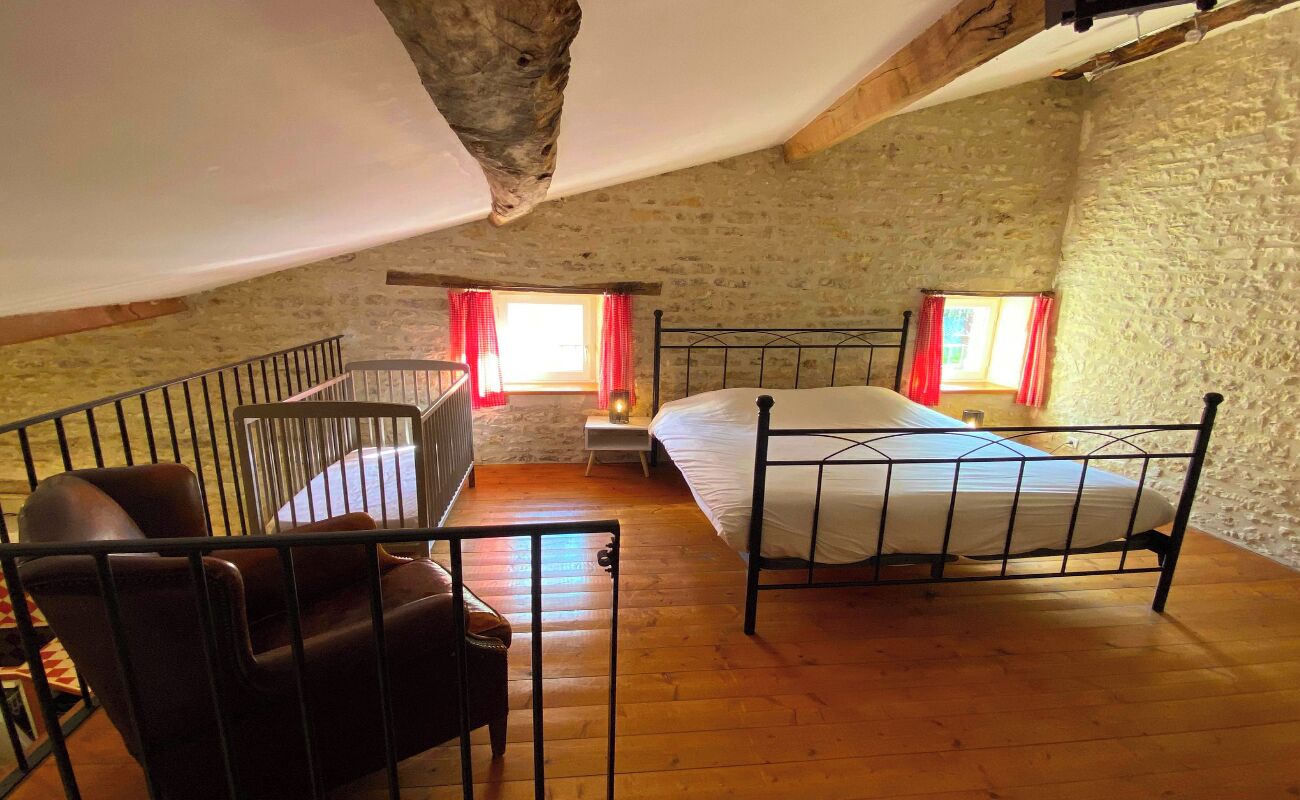 A loft bedroom with a sloped ceiling, two beds, a wooden floor, and a stone wall.