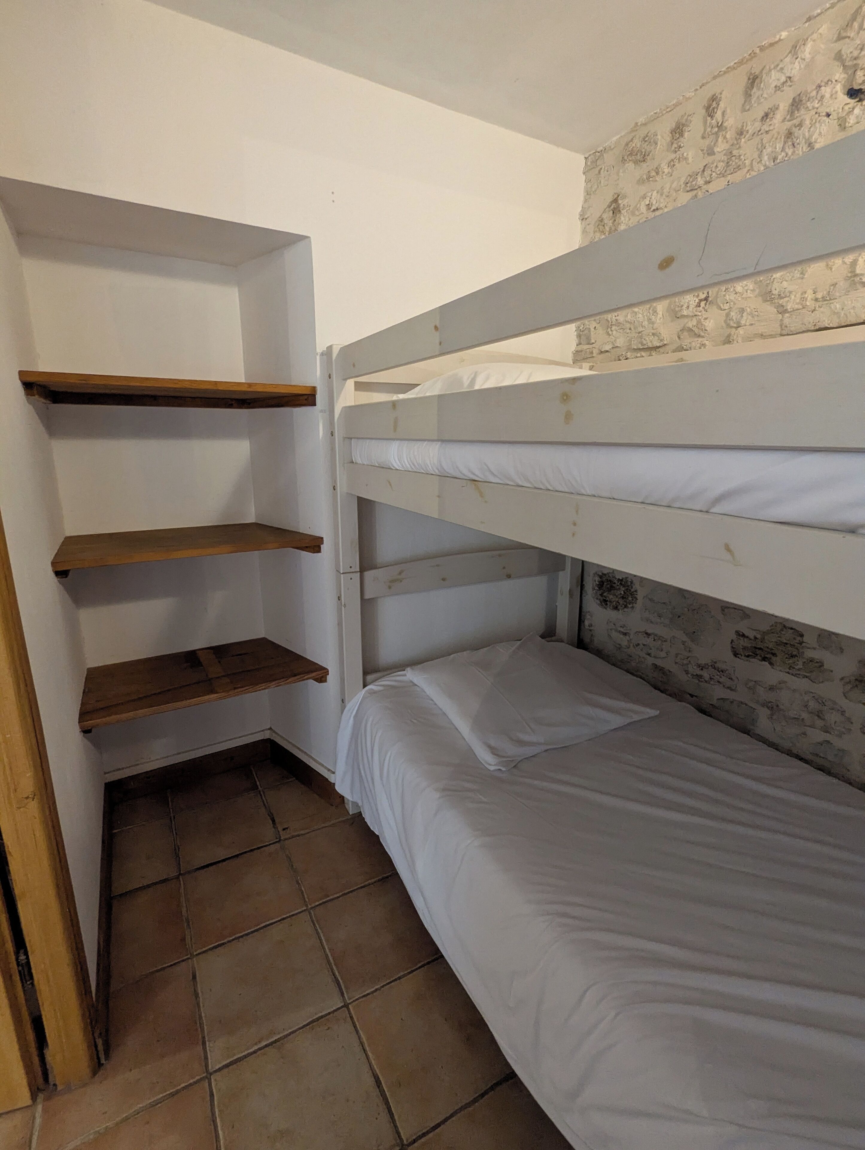Een stapelbed met twee niveaus, houten planken en een betegelde vloer.