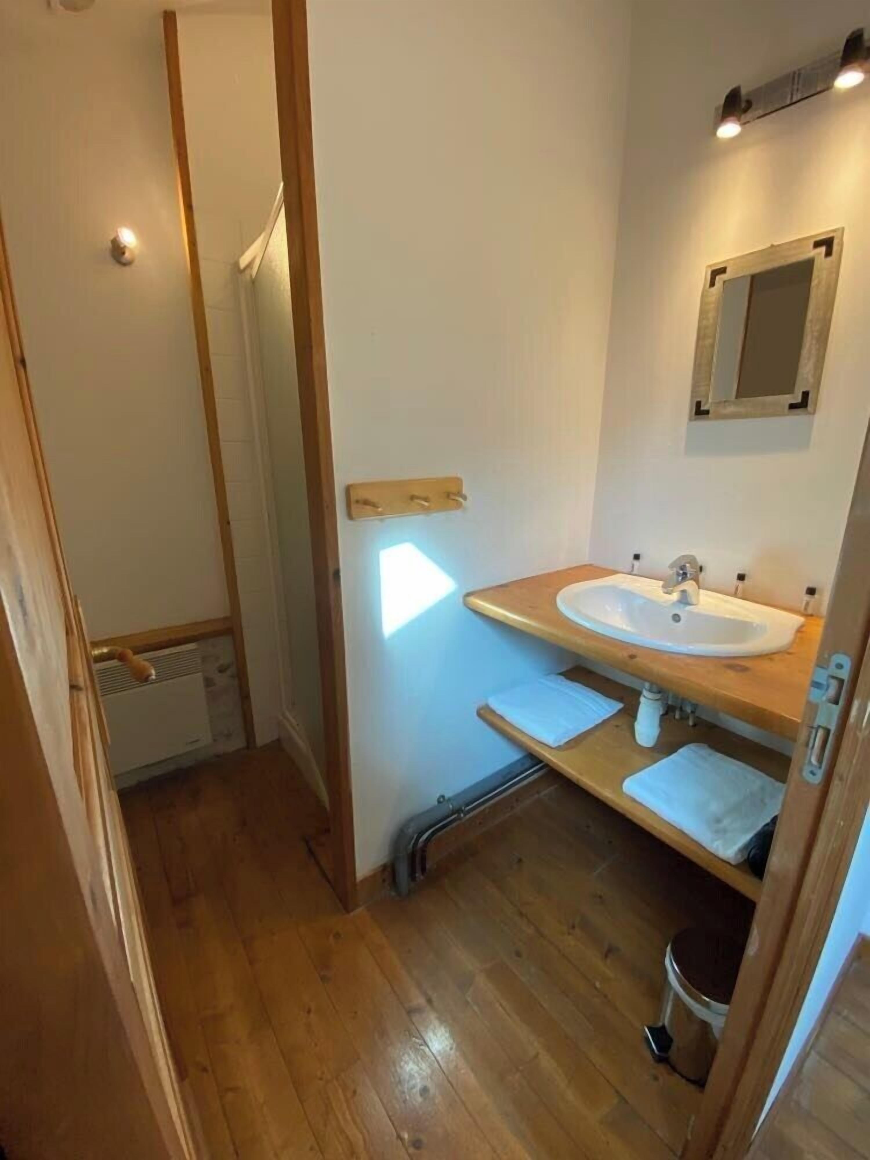 Een compacte badkamer met een houten vloer, een witte wastafel, een spiegel en een handdoekhouder.