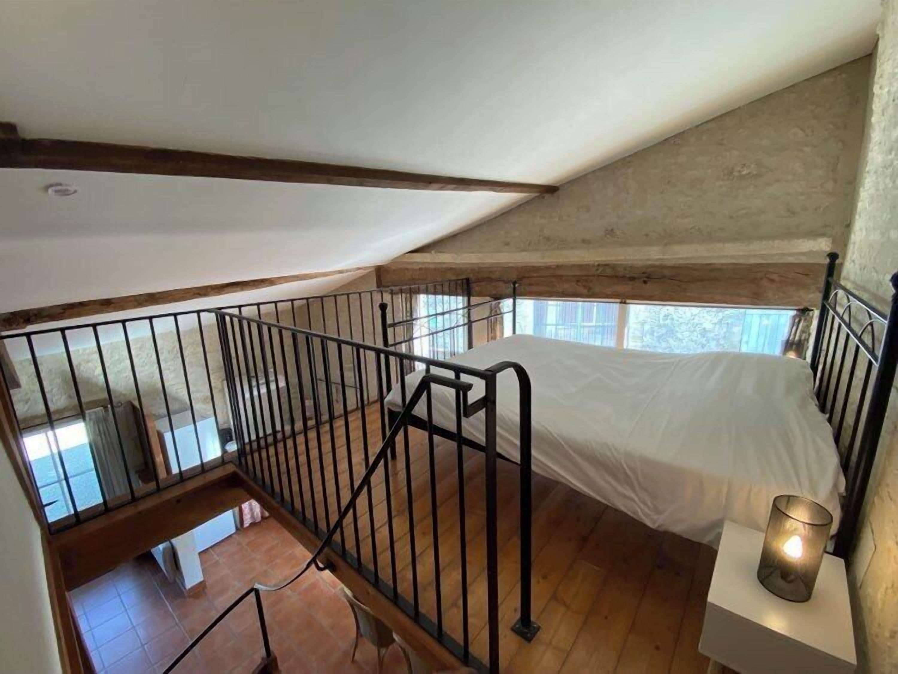 Ein Schlafzimmer mit Holzboden, einem weißen Bett, einem Metallgeländer und einem Nachttisch mit Kerze.
