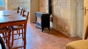 Een rustiek interieur met zichtbare stenen muren, een houten plafond, een open haard en een eethoek met stoelen en een tafel.