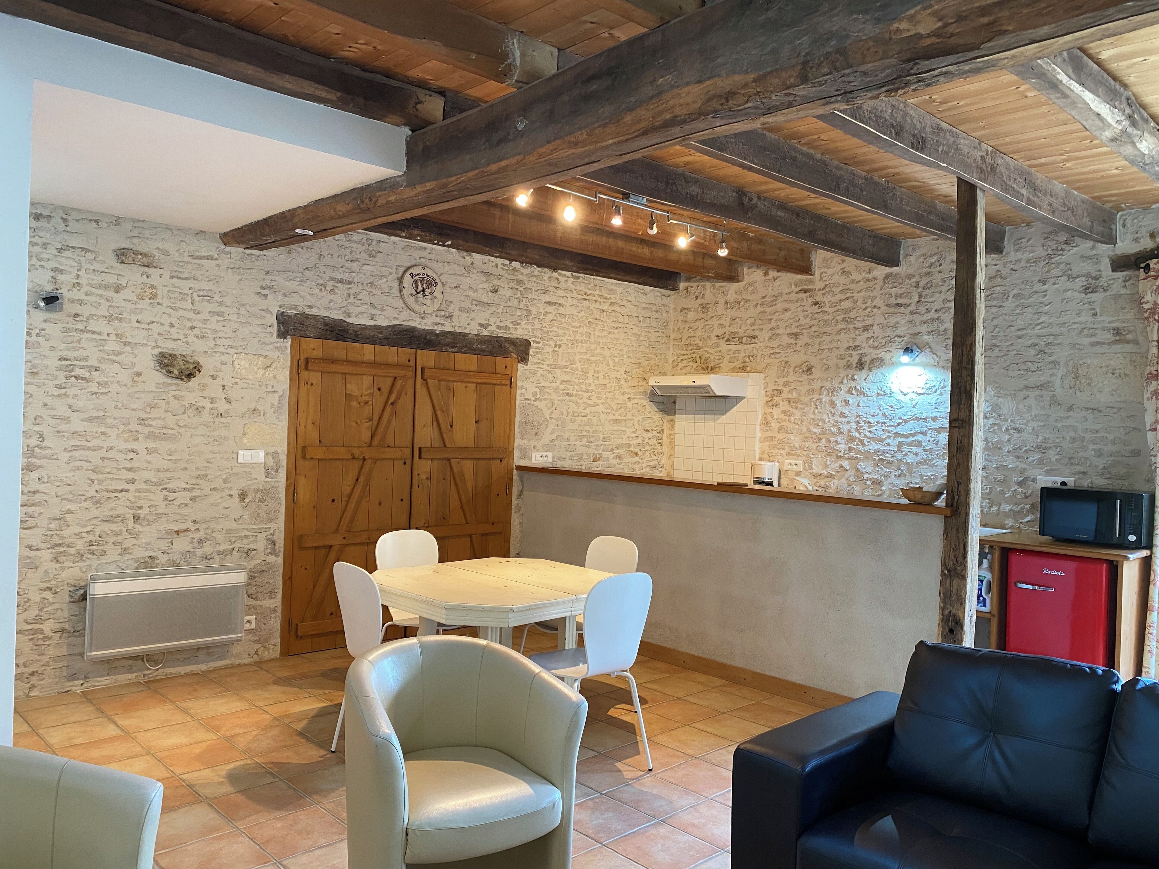 A rustic dining area with a stone wall, wooden beams, a round table, and white chairs.