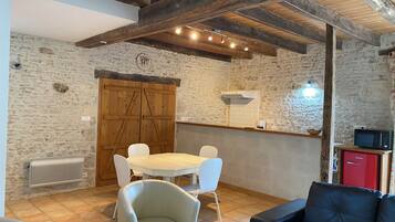 A rustic dining area with a stone wall, wooden beams, a round table, and white chairs.