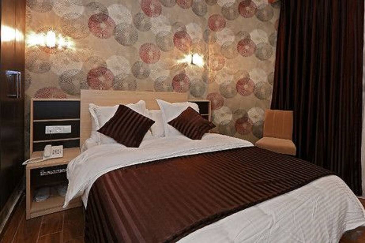 A hotel room with a large bed, two bedside tables, a nightstand, a wall-mounted lamp, and a patterned wallpaper.